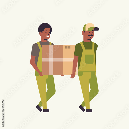 two couriers in uniform carrying cardboard box package mail express delivery service concept african american workers holding parcel flat full length