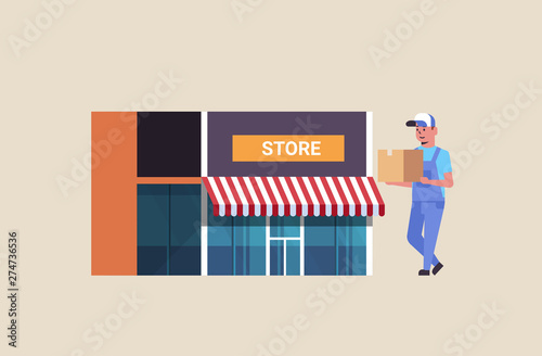 postman in uniform carrying cardboard parcel box courier express delivery service concept modern store building exterior flat full length horizontal
