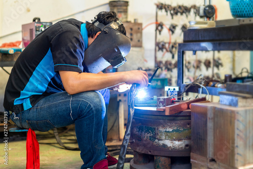 worker or welder wearing a mask for protect light and smoke during welding metal part or workpiece at factory and sparkle bright right