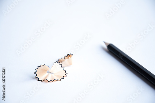 black pencil lies on the table. Nearby is shavings from a pencil. On a white background