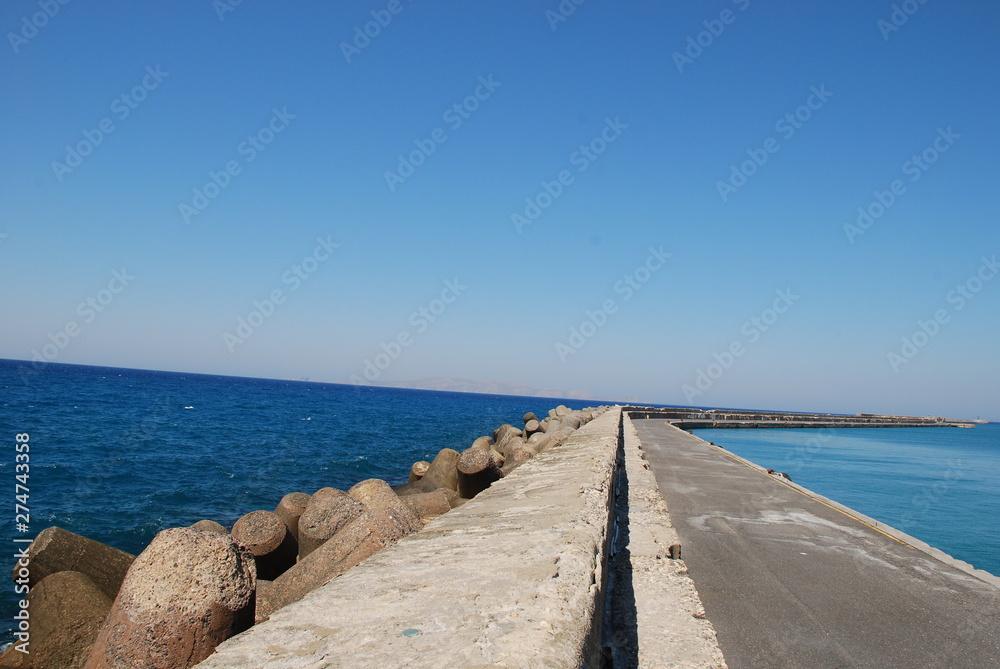Long stone pier stretching into the blue sea