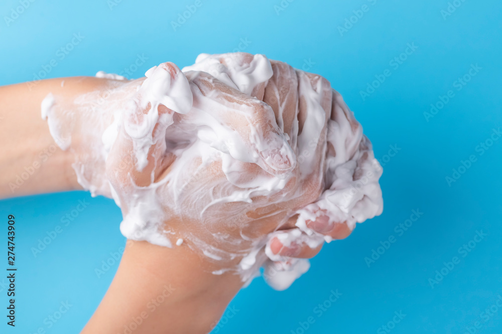 Teenager washes his hands with foam soap on a blue bright background