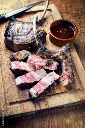 Barbecue dry aged Tomahawk Schweine Steak aufgeschnitten als Draufsicht auf einem alten rustikalen Schneidebrett mit scharfer Grill Sauce