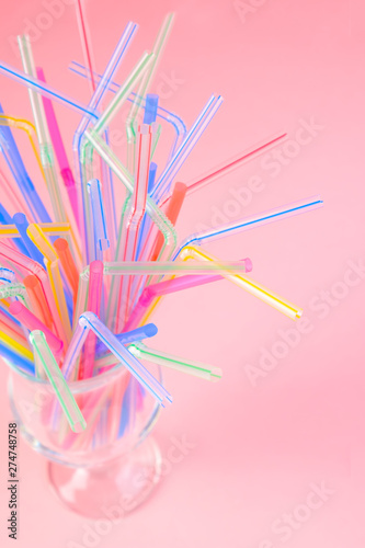 Multicolored plastic cocktail straws in an empty glass cup on a pink background. Concept: holiday, party, ecology, plastic