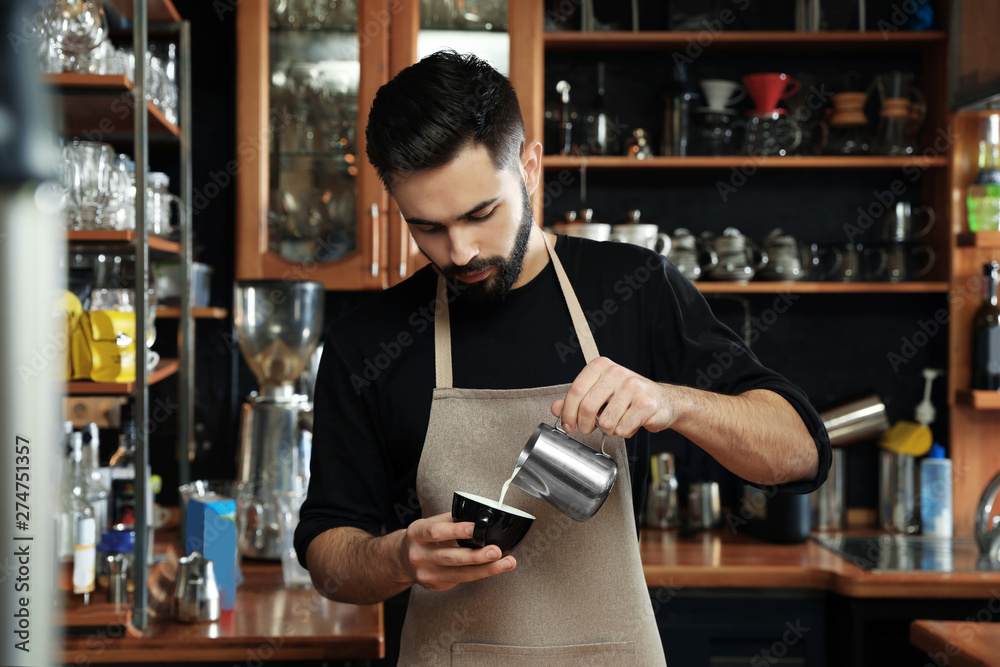 Portrait of barista pouring milk into cup of coffee against bar shelves in cafe
