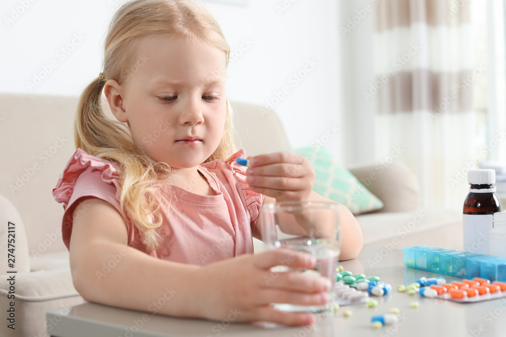 Little child taking pill at table indoors. Danger of medicament intoxication Little child taking pill at table indoors. Danger of medicament intoxication