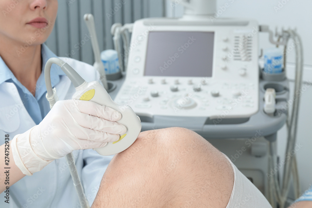 Doctor conducting ultrasound examination of patient's knee in clinic Doctor conducting ultrasound examination of patient's knee in clinic