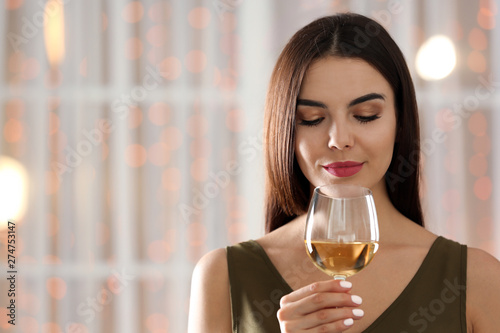 Beautiful young woman with glass of luxury white wine indoors. Space for text