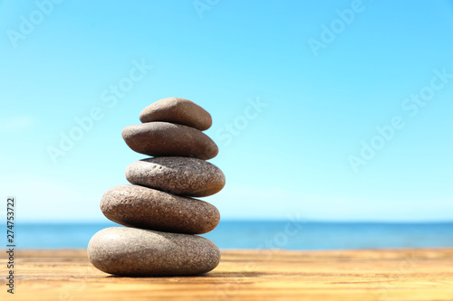 Stack of stones on wooden table against seascape, space for text. Zen concept