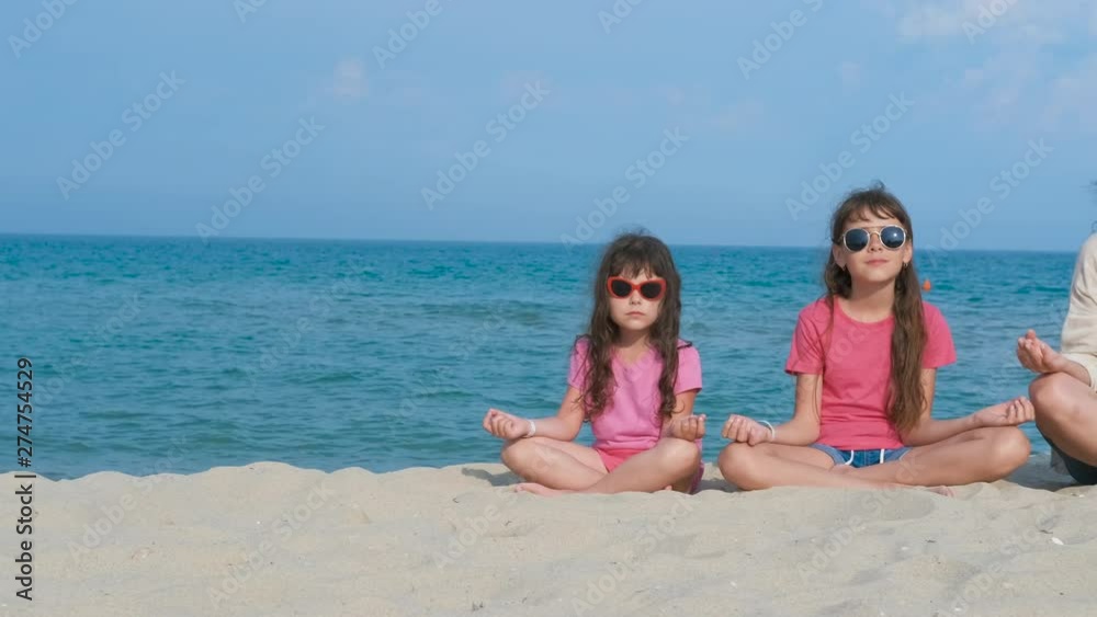 Family doing yoga. Mother with daughters in the lotus position on the sand against the backdrop of the sea. Family doing yoga. Mother with daughters in the lotus position on the sand against the backdrop of the sea.