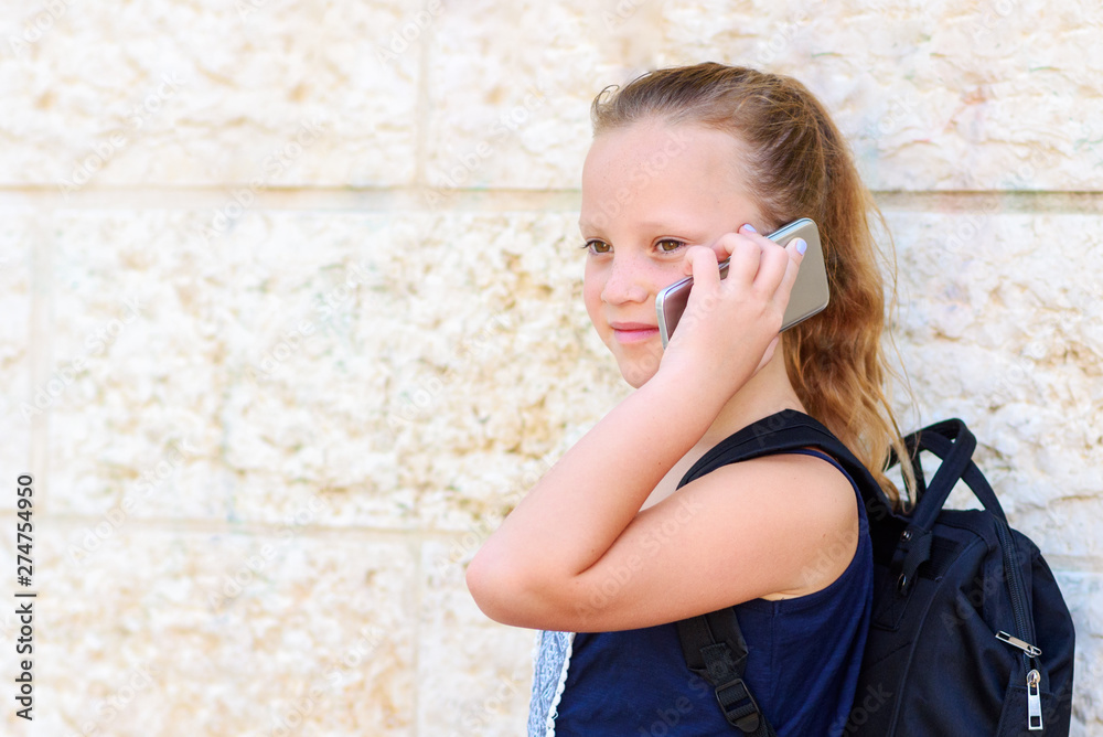 Outdoor portrait of happy girl 8-9 year old talking on phone. Cute schoolgirl with backpack talking on cell phone and smiling. Outdoor portrait of happy girl 8-9 year old talking on phone. Cute schoolgirl with backpack talking on cell phone and smiling.