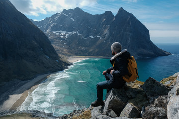 Man sitting on cliff edge alone enjoying aerial view backpacking lifestyle travel adventure outdoor vacations in Norway top of Reinebringen mountain.