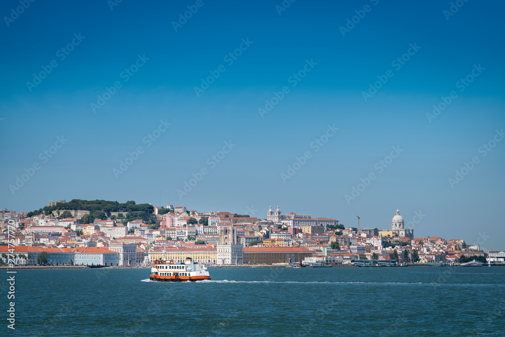 A traditional ferry boat (Cacilheiro) crossing the Tagus River with the Lisbon skyline on the background.