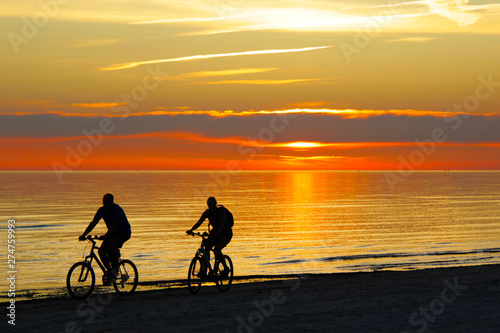 couple riding a bicycles and sunset over the sea on background
