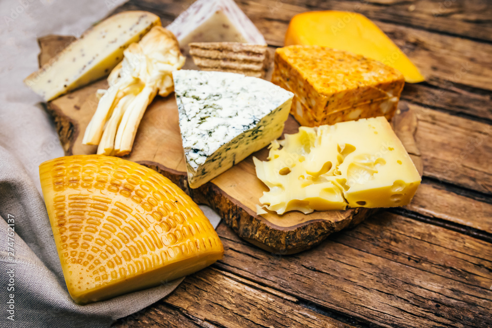 Assorted, various aged cheeses on plate or wooden board. Different kind or type of delicious cheese on cheese platter. 