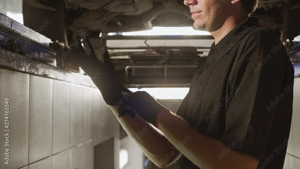 Mechanic stands in the car pit and wears glover before making repair