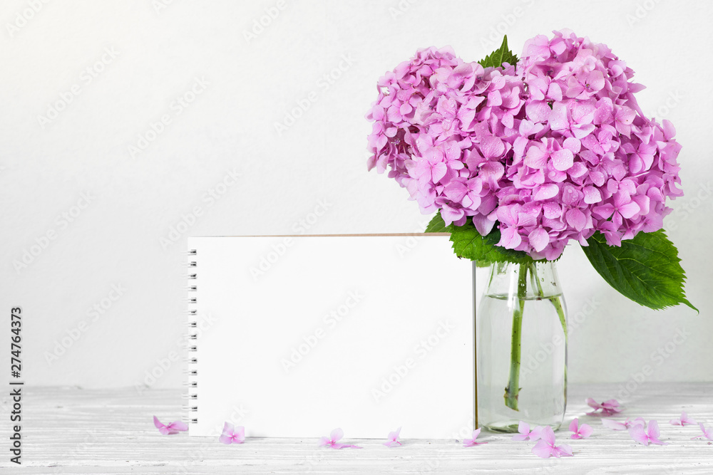 Obraz premium Modern still life with a beautiful pink hydrangea flowers and blank paper card on white wooden table