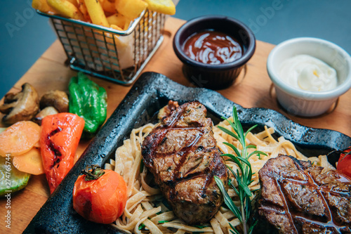 Grilled or roasted beef steak meat and pasta food meal with french fries potatoes in cafe or restaurant. Dinner or lunch table concept image