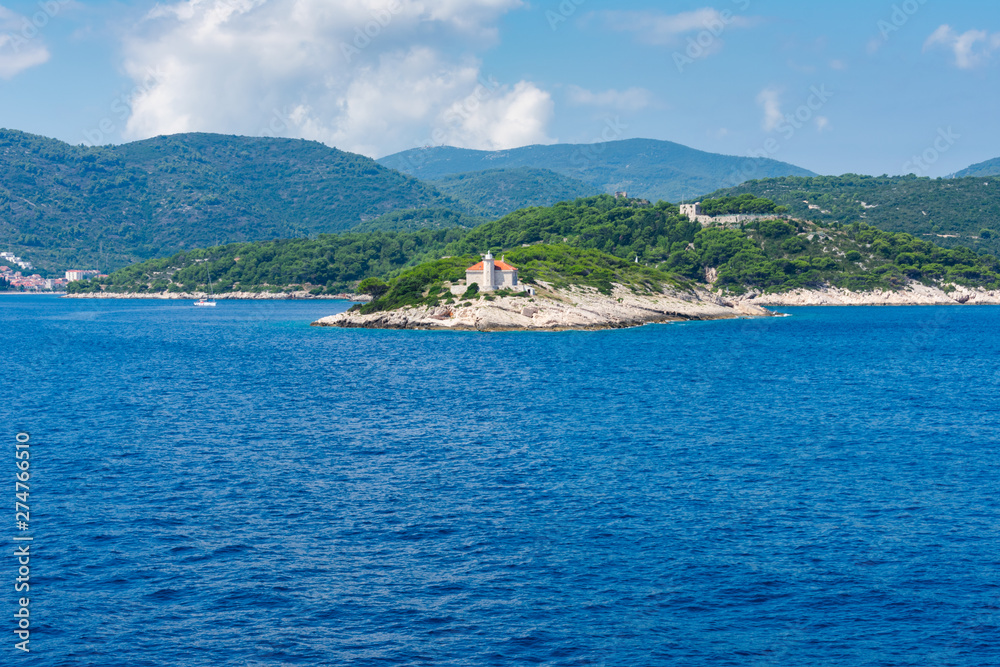 Seascape view of a small lighthouse on a green peninsula at the entrance of city of Vis harbour in Croatia, on a bright summer day