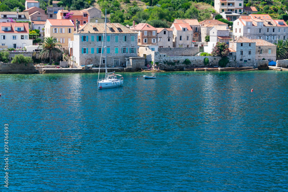 Old city of Vis viewed from the sea entering the harbor with old stone houses with red rooftops and sailing boats anchored in summer, Vis island, Croatia