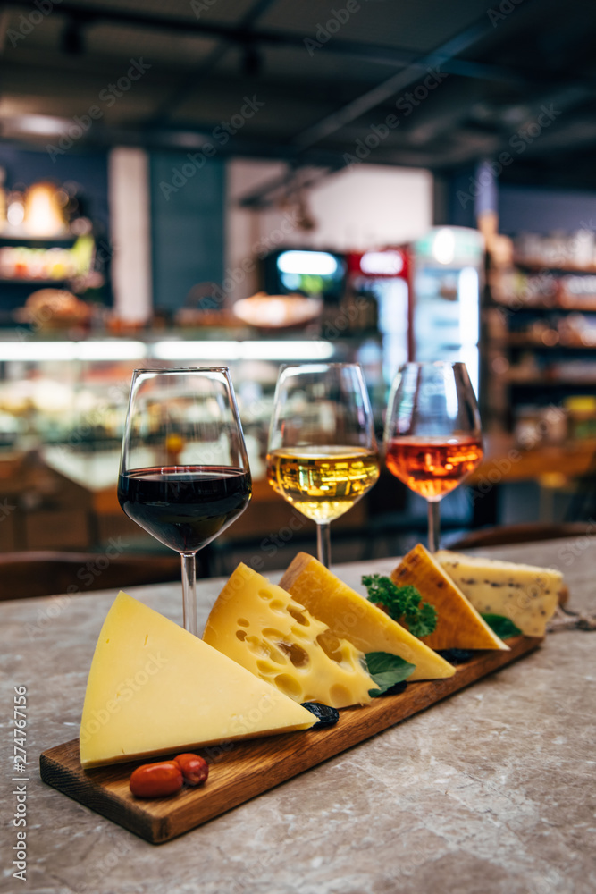 Glasses of Wine and cheese. Assortment or various type of cheese and wine glasses on the table in restaurant. Red, rose and yellow wine or champagne on the table. Winery concept image