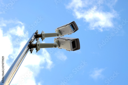Surveillance cameras seen from below with sky background.