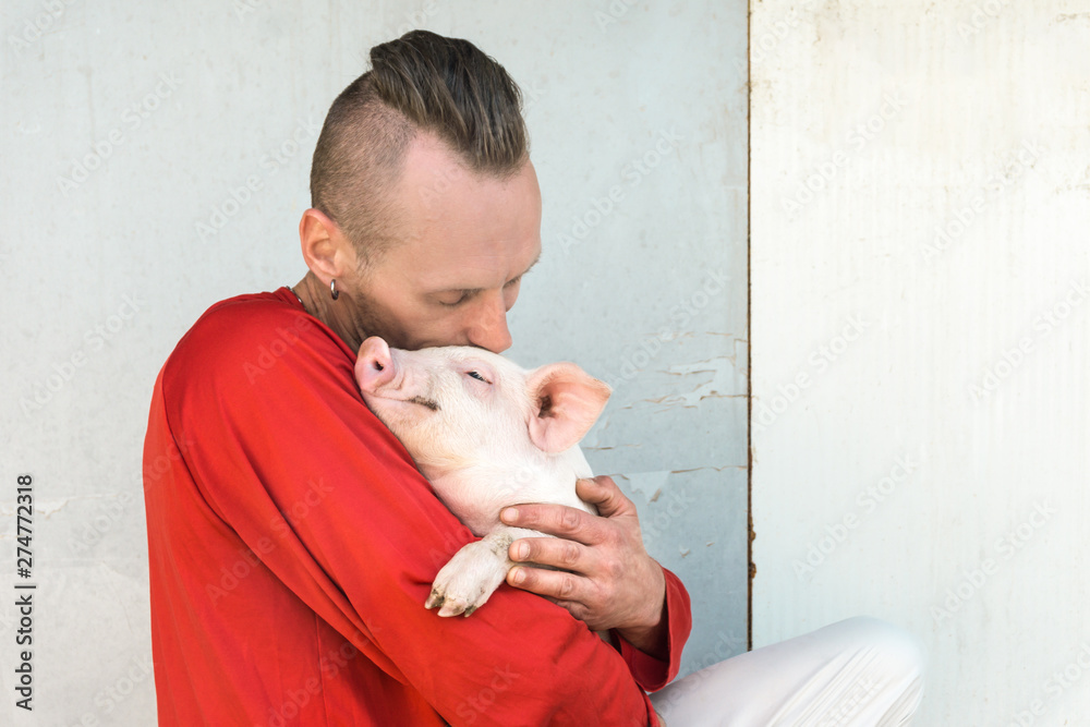Pig farmer with cute piglet in hands at farm wall. Focus on piggy. Pig farmer with cute piglet in hands at farm wall. Focus on piggy.