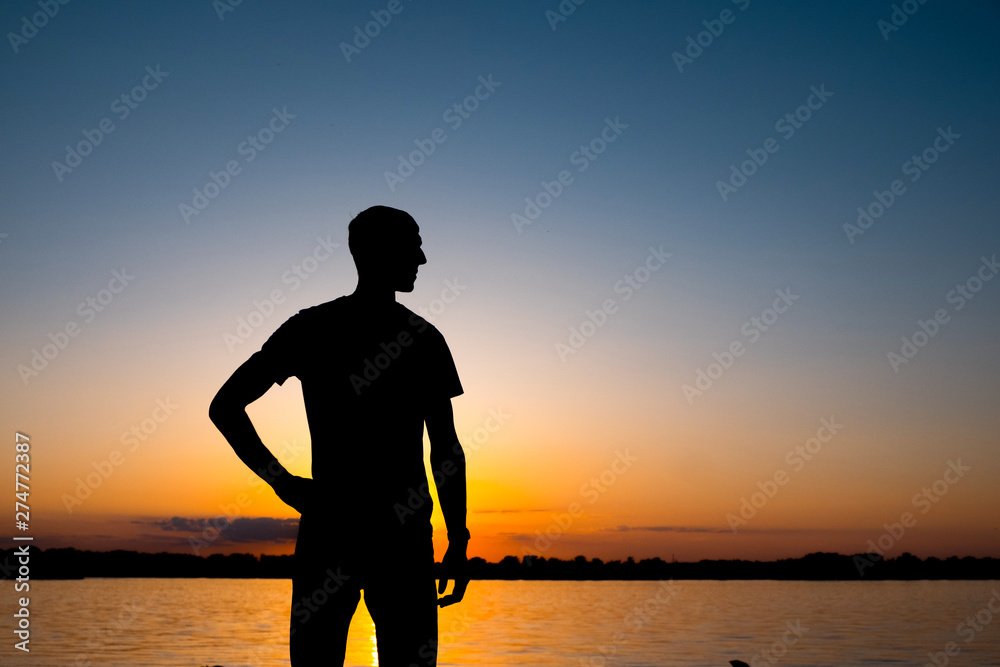 The young man is standing before the river bank with yesllow - blue Sunrise or sunset