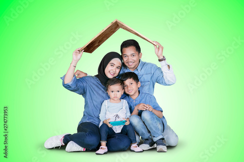 Smiling family sits under a roof symbol on studio © Creativa Images
