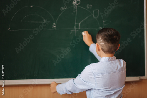 Little boy white down something on blackboard. Clever male