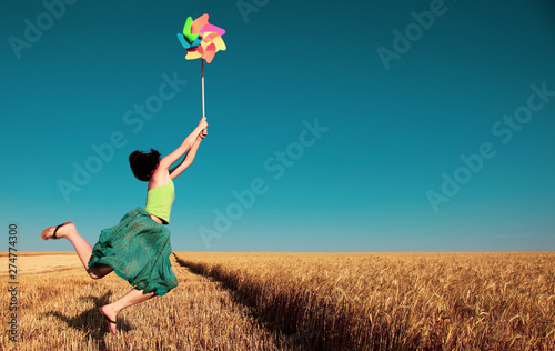 Papier peint Young girl jumping with pinwheel over wheat field