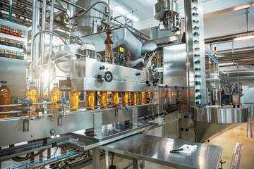 Conveyor belt or line in beverage plant with modern automated industrial machine equipment. Plastic PET bottles with fresh organic juice in factory interior