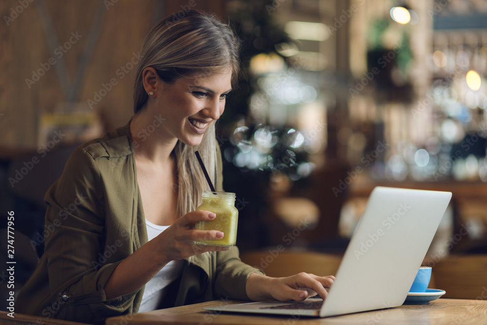 Happy woman using laptop while drinking smoothie in a cafe Happy woman using laptop while drinking smoothie in a cafe