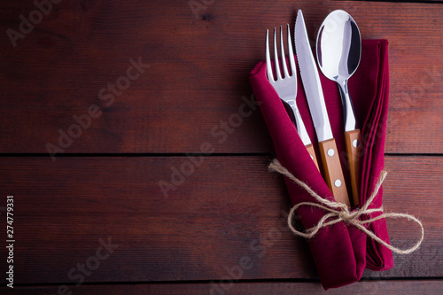 Rustic set of cutlery knife, spoon, fork. Сutlery with burgundy napkin and twine. Wooden background. Copy space. Top view