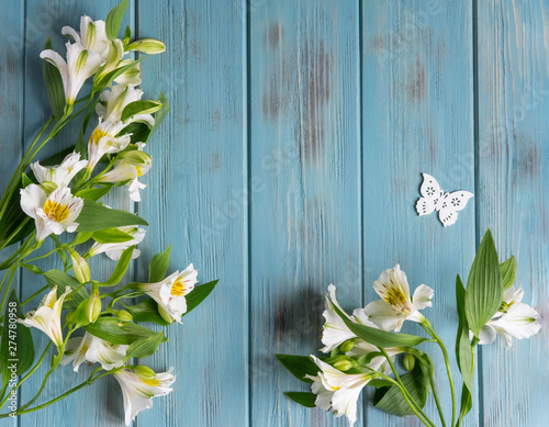 Background for text banner on a blue wooden background with white flowers and butterflies. Blank, frame for text. Greeting card design with flowers. Alstroemeria on wooden background. View from above