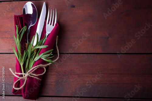 Set of cutlery knife, spoon, fork. Сutlery with burgundy napkin and twine. Rosemary on wooden background. Copy space. Top view