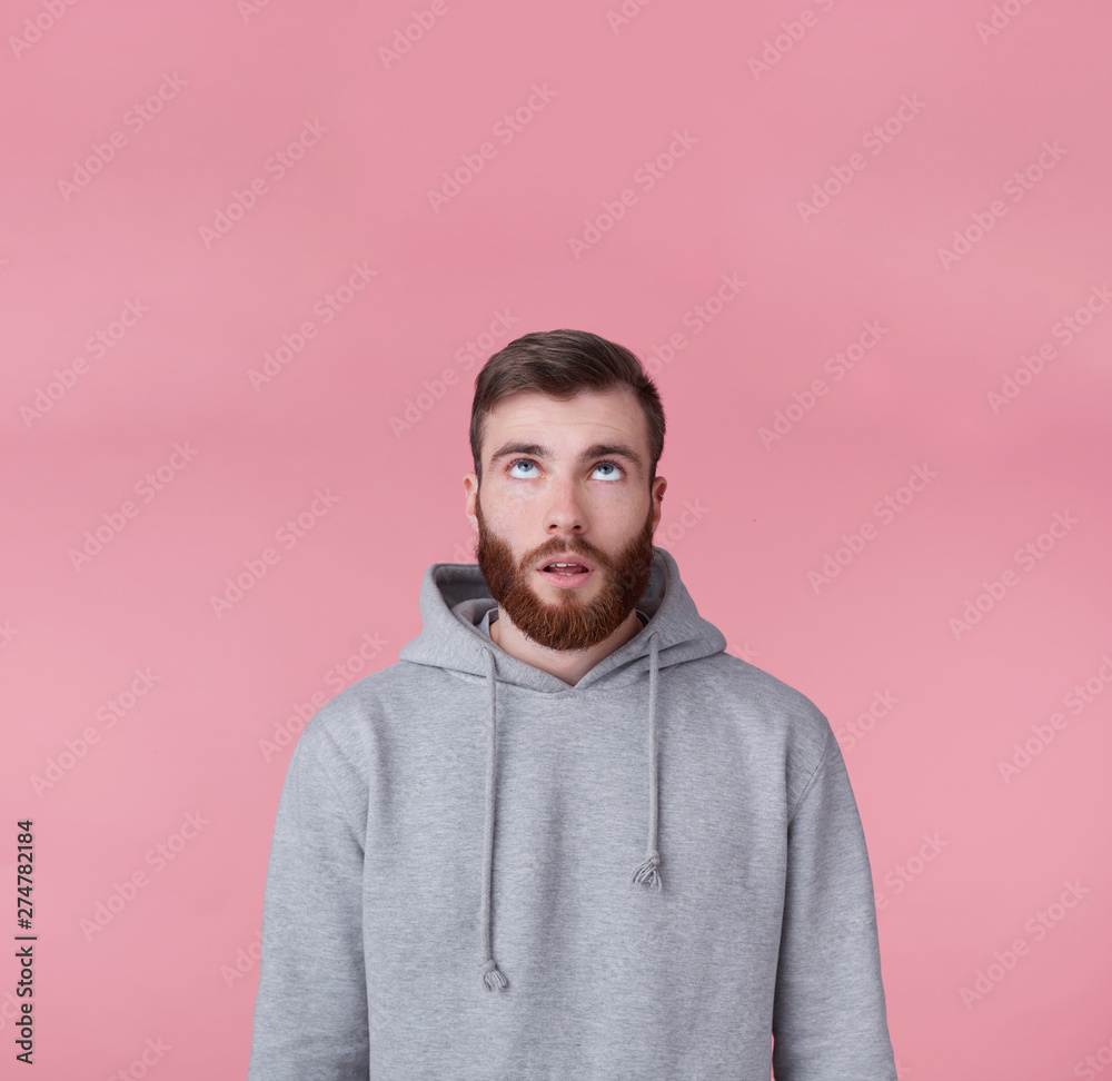 Portrait of young tired handsome guy looking up at the copy space, thinking about solving a problem, presents possible options, stands over pink background. Portrait of young tired handsome guy looking up at the copy space, thinking about solving a problem, presents possible options, stands over pink background.