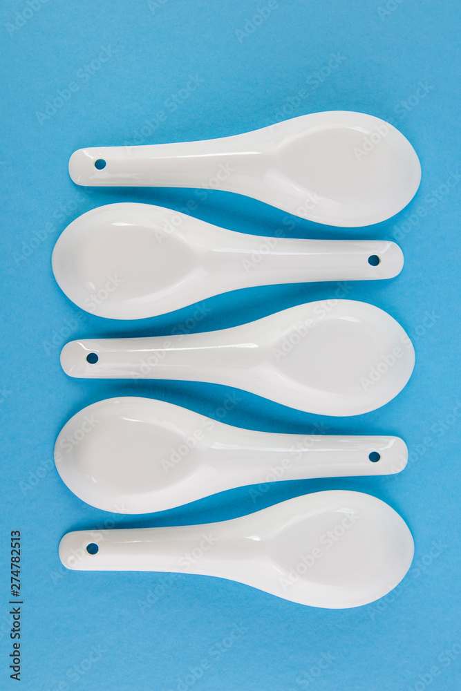 White Asian style spoons arranged in geometric pattern on blue background White Asian style spoons arranged in geometric pattern on blue background