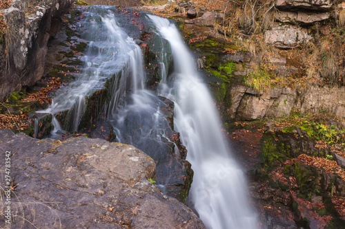 Gorgeous mountain creek waterfall cascading down the rocky cliff and colorful autumn red leaves  close-up
