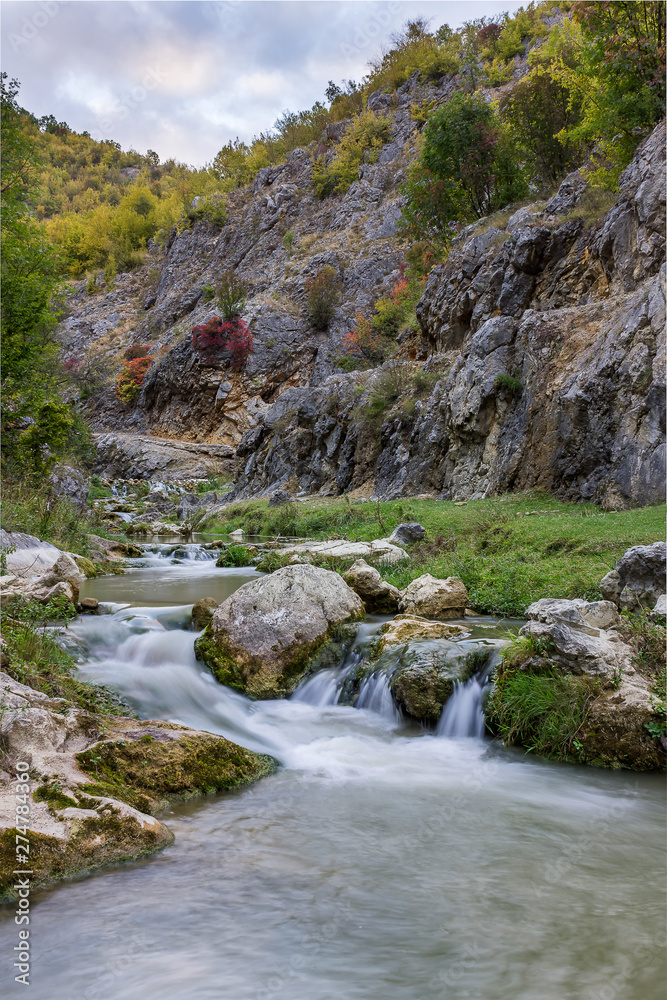 Amazing autumn color palette of the trees in a narrow canyon with mountain creek cascades