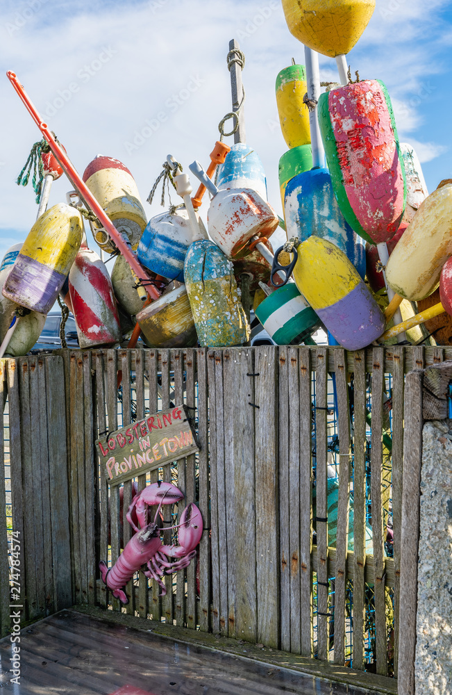 Fototapeta premium Lobstering in Provincetown sign on a weathered wood bench with many multi colored buoy floats behind