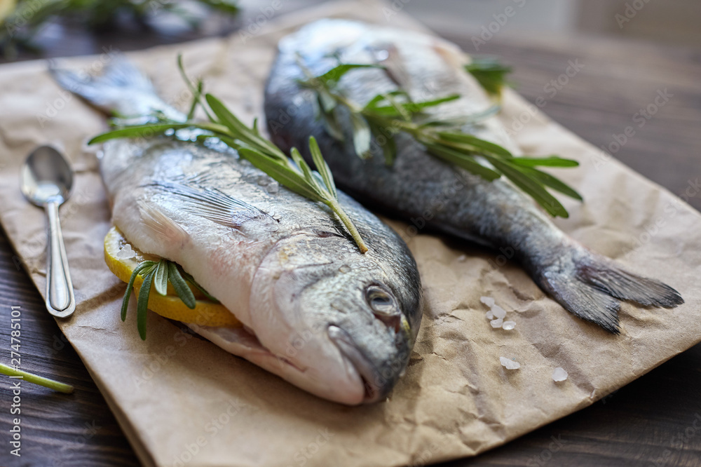 Fresh uncooked dorado or sea bream fish with lemon, herbs, oil, vegetables and spices on rustic wooden board over black backdrop, top view Fresh uncooked dorado or sea bream fish with lemon, herbs, oil, vegetables and spices on rustic wooden board over black backdrop, top view