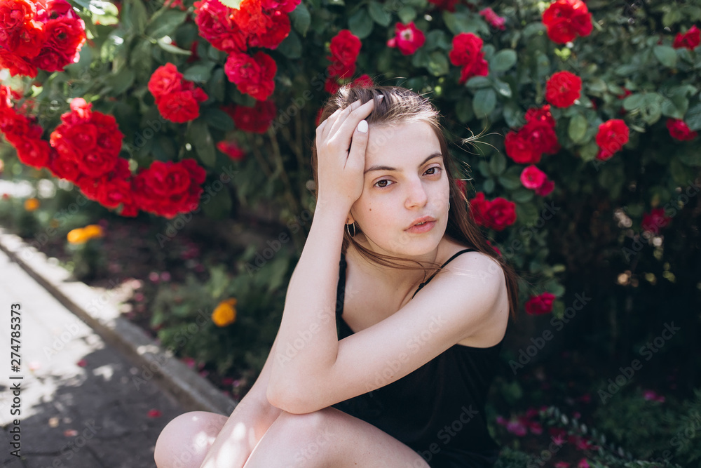 Close up summer portrait of young sensual interesting pretty young woman outdoors near red roses. Modeling, fashion, trends, nature concept Close up summer portrait of young sensual interesting pretty young woman outdoors near red roses. Modeling, fashion, trends, nature concept