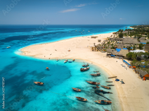 Aerial view of the fishing boats on tropical sea coast with sandy beach at sunny day. Summer holiday on Indian Ocean, Zanzibar, Africa. Landscape with boat, buildings, transparent blue water. Top view