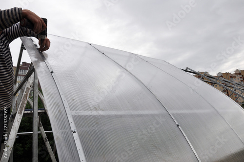 installation of domed greenhouses on the ground, consisting of steel profiles and plastic. In the background there is a Church, private and multi-storey buildings.