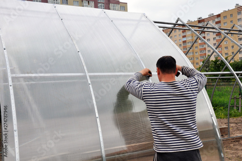 installation of domed greenhouses on the ground, consisting of steel profiles and plastic. In the background there is a Church, private and multi-storey buildings.