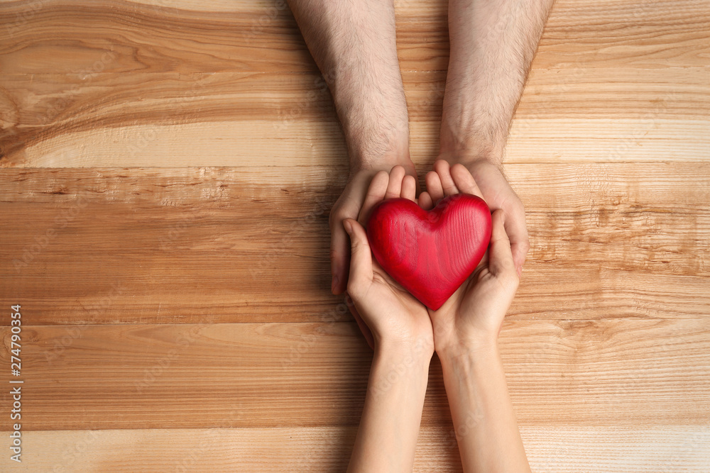 Couple holding decorative heart on wooden background, top view Couple holding decorative heart on wooden background, top view