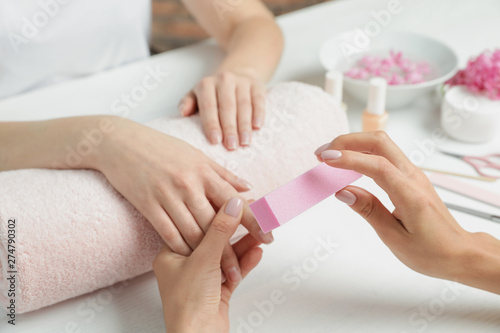 Manicurist polishing client's nails with buffer at table, closeup. Spa treatment photo