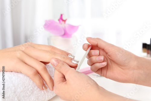 Manicurist filing client s nails covered with polish in salon  closeup