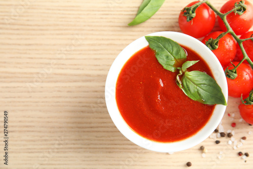 Bowl of tasty tomato sauce with basil on wooden table, flat lay. Space for text